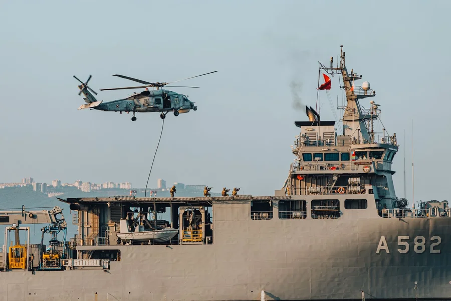 Naval recovery ship sailing open ocean with support helicopter