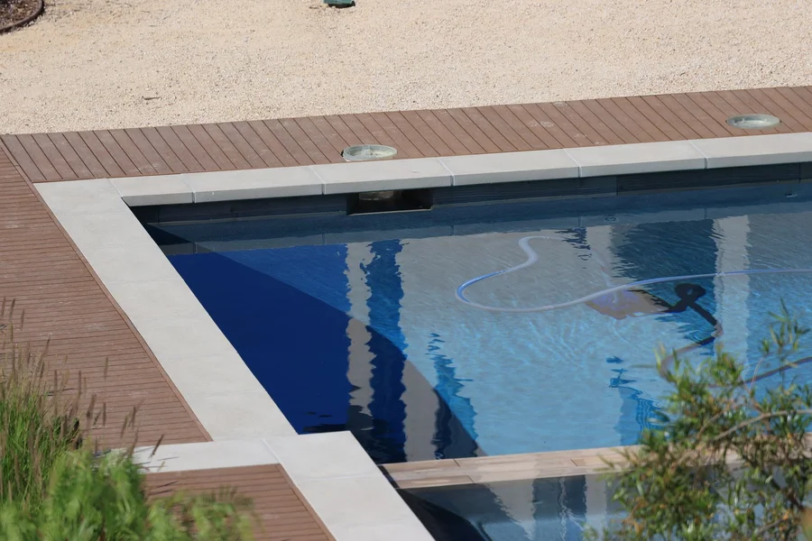 Pool technician vacuuming the bottom of a backyard swimming pool